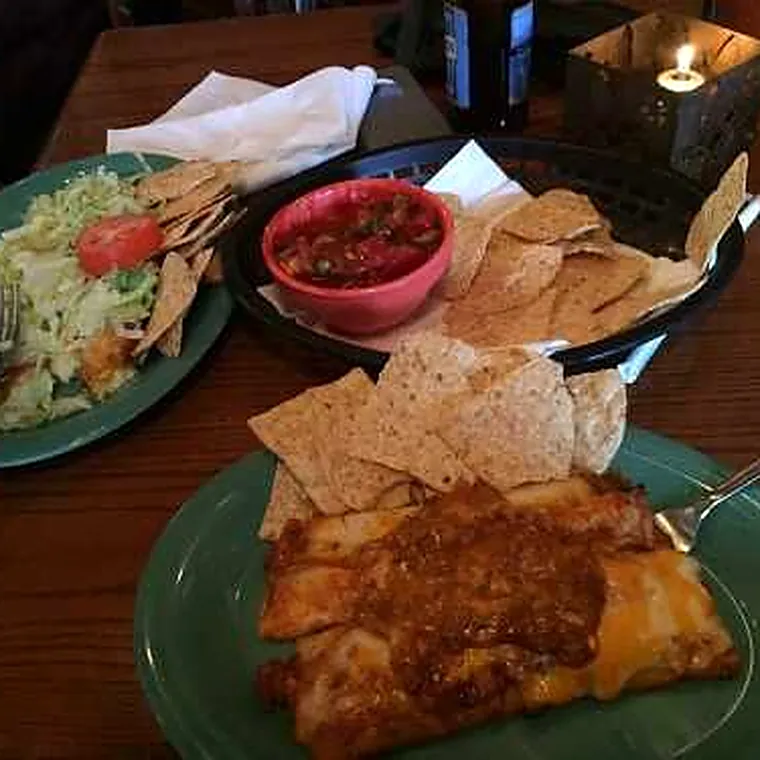 An enchilada with a side salad, chips and a bowl of salsa