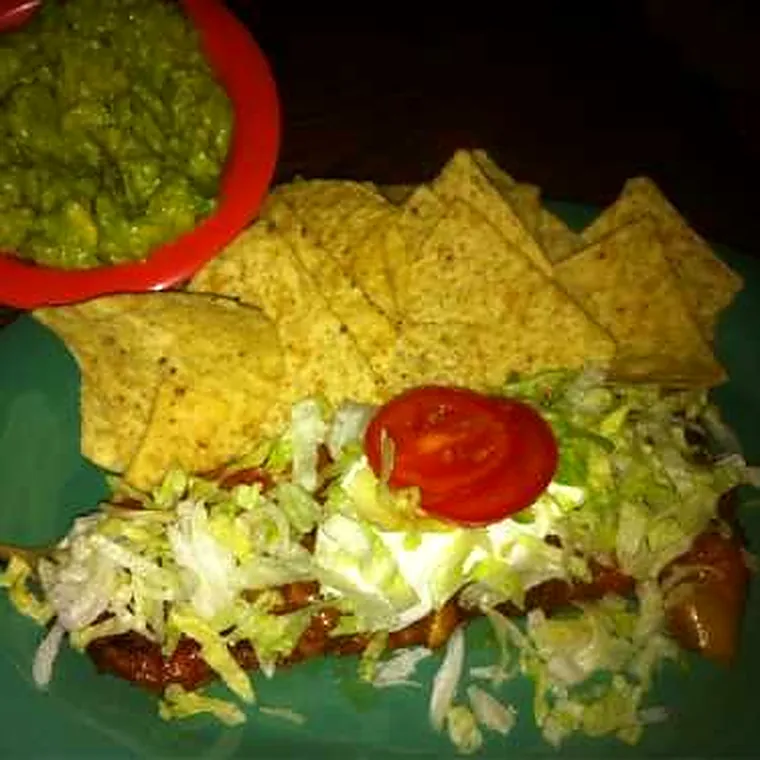 Guacamole in a red bowl beside an enchilada and chips