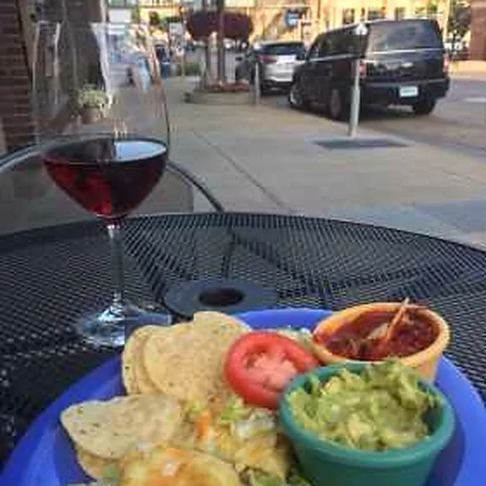 A plate and a glass of red wine on a table outside on West 11th